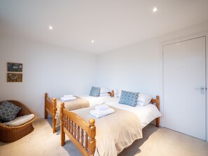 A bedroom with two wooden beds, a wicker chair, and a door.