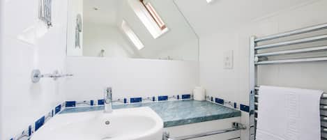 A bathroom with a skylight, a sink, a mirror, and a towel rack.