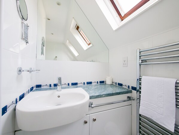 A bathroom with a skylight, a sink, a mirror, and a towel rack.