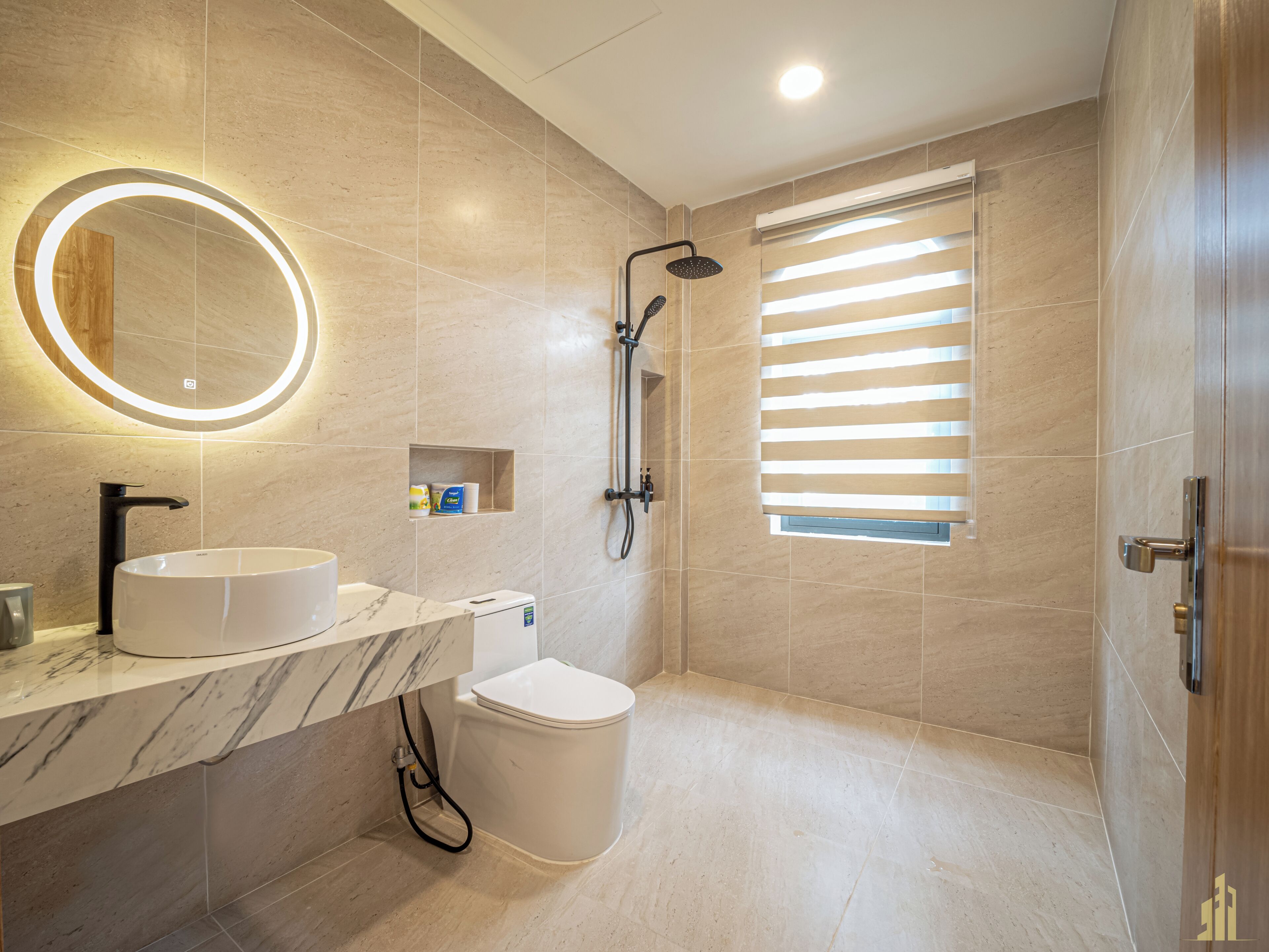 A modern bathroom with a marble vanity, a toilet, a shower with a handheld showerhead, and a window with blinds.