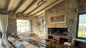 Un intérieur rustique avec des murs en pierre, une cheminée et un coin salon confortable avec un canapé et des fauteuils.