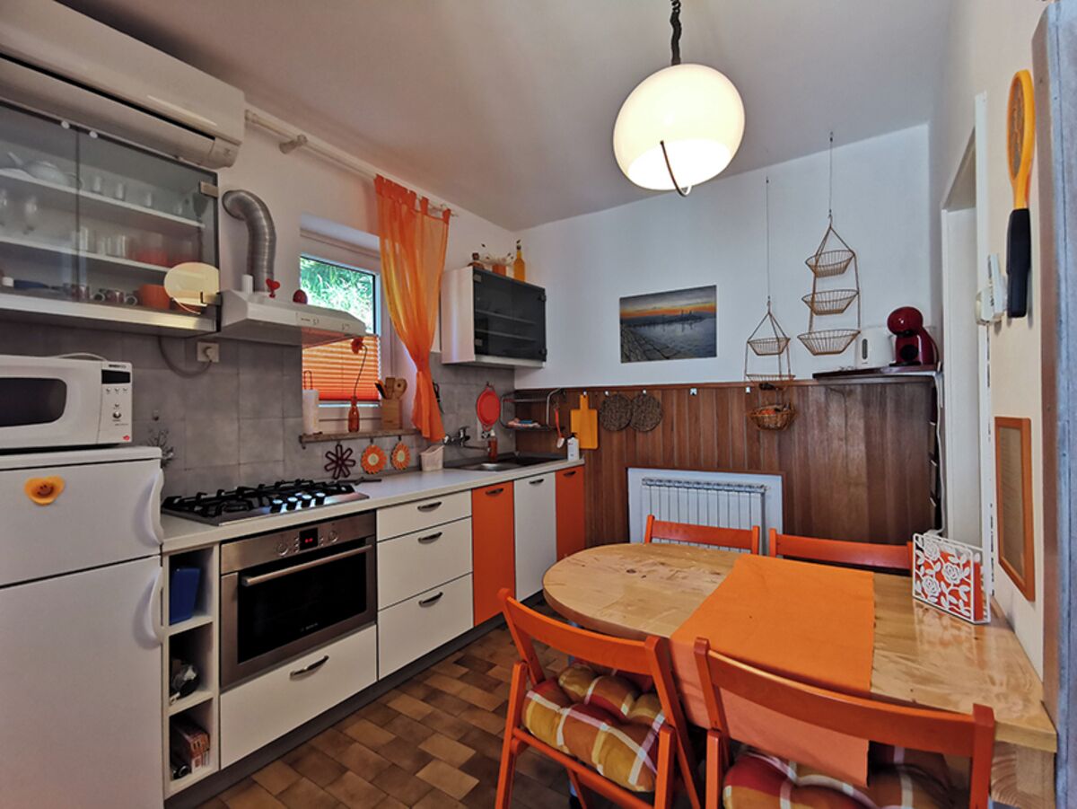 A compact kitchen with white and orange cabinetry, a wooden dining table, and a hanging light fixture.
