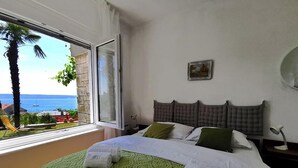 Habitación de hotel con cama, ventana con vista al mar, un cuadro en la pared y una lámpara en la mesita de noche.