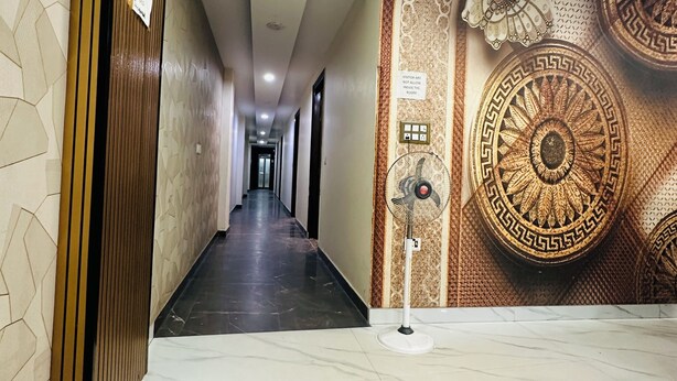 A hotel corridor with a marble floor, a wooden panel wall, and a decorative wall with a large circular design. - Hotel S R Palace Unit BY Urban Luxury (New Delhi)