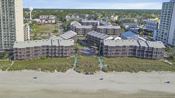 A coastal hotel complex with multiple buildings, a beach in the foreground, and a clear sky. - Tilghman 232- Ocean Drive- 3BR/2.5BA (North Myrtle Beach)