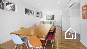 A modern kitchen with white cabinets, a wooden dining table, and colorful chairs. - Banksia Beach Retreat *1 NIGHT FREE* (Blairgowrie)