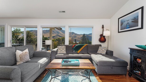 A modern living room with a gray sectional sofa, a wooden coffee table, and a view of mountains through large windows. - Park Pointe B302- Community Pool and Hot Tub! (Chelan)