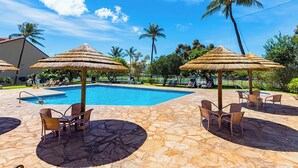 Ein Poolbereich mit Reetsonnenmatten, Liegestühlen und Palmen.