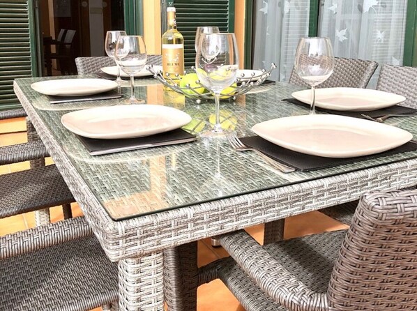 Mesa de comedor preparada con platos, vasos y una botella, rodeada de sillas de mimbre.