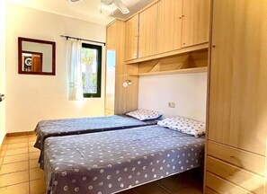 A bedroom with two beds, wooden wardrobe, and a window with curtains. - Villa- Sleep6- Private Pool and hot tub (La Oliva)