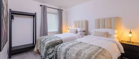 Camera d'albergo con due letti, un'ampia finestra con tende, un lampadario e un comodino con lampada.