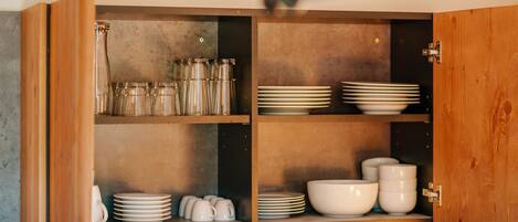 Un mueble de madera con puertas de cristal, que contiene varios utensilios de cocina como frascos de vidrio, platos y tazones.