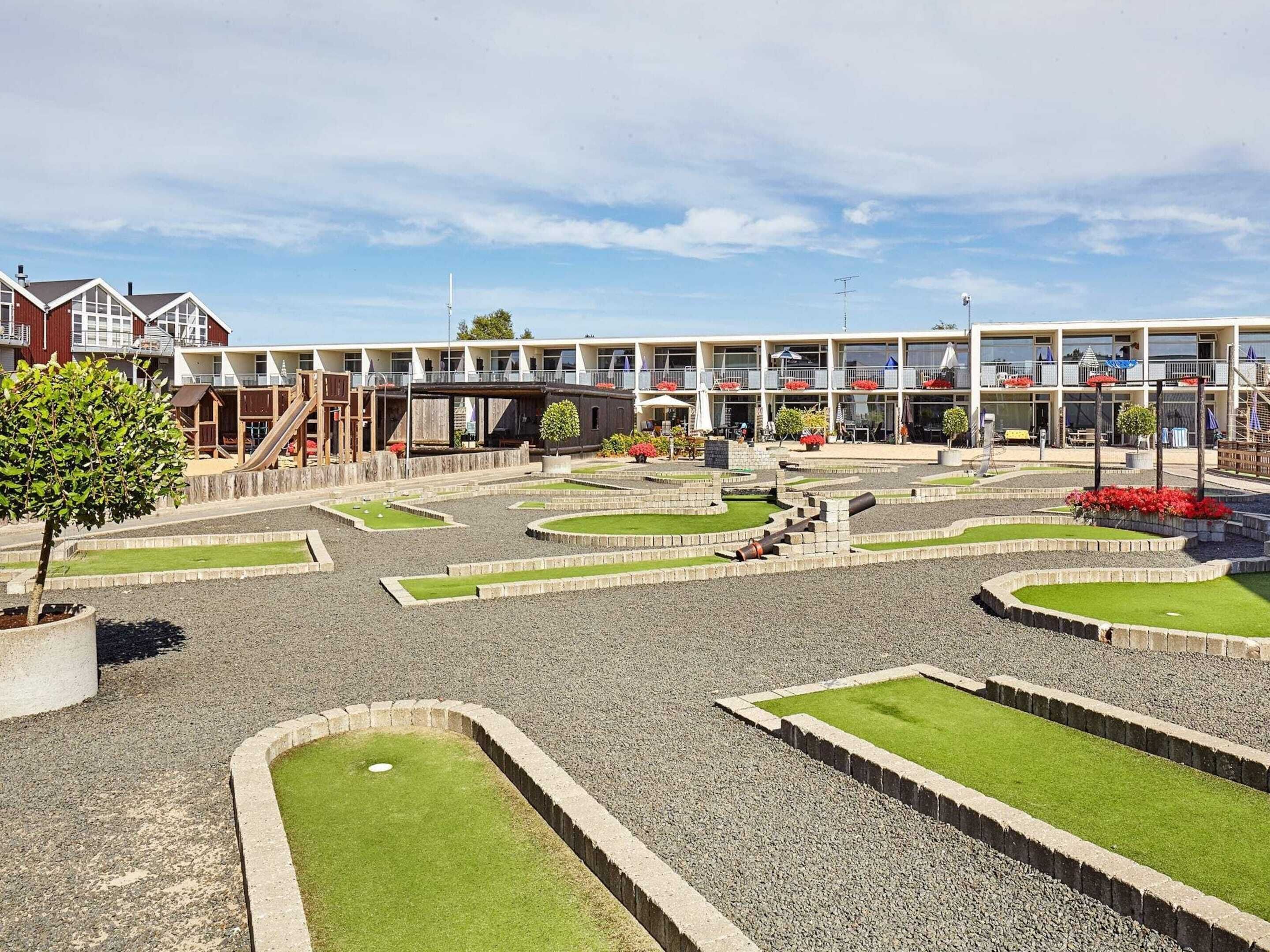 Un patio con zona de juegos infantiles, un edificio con varios balcones y un cielo despejado.