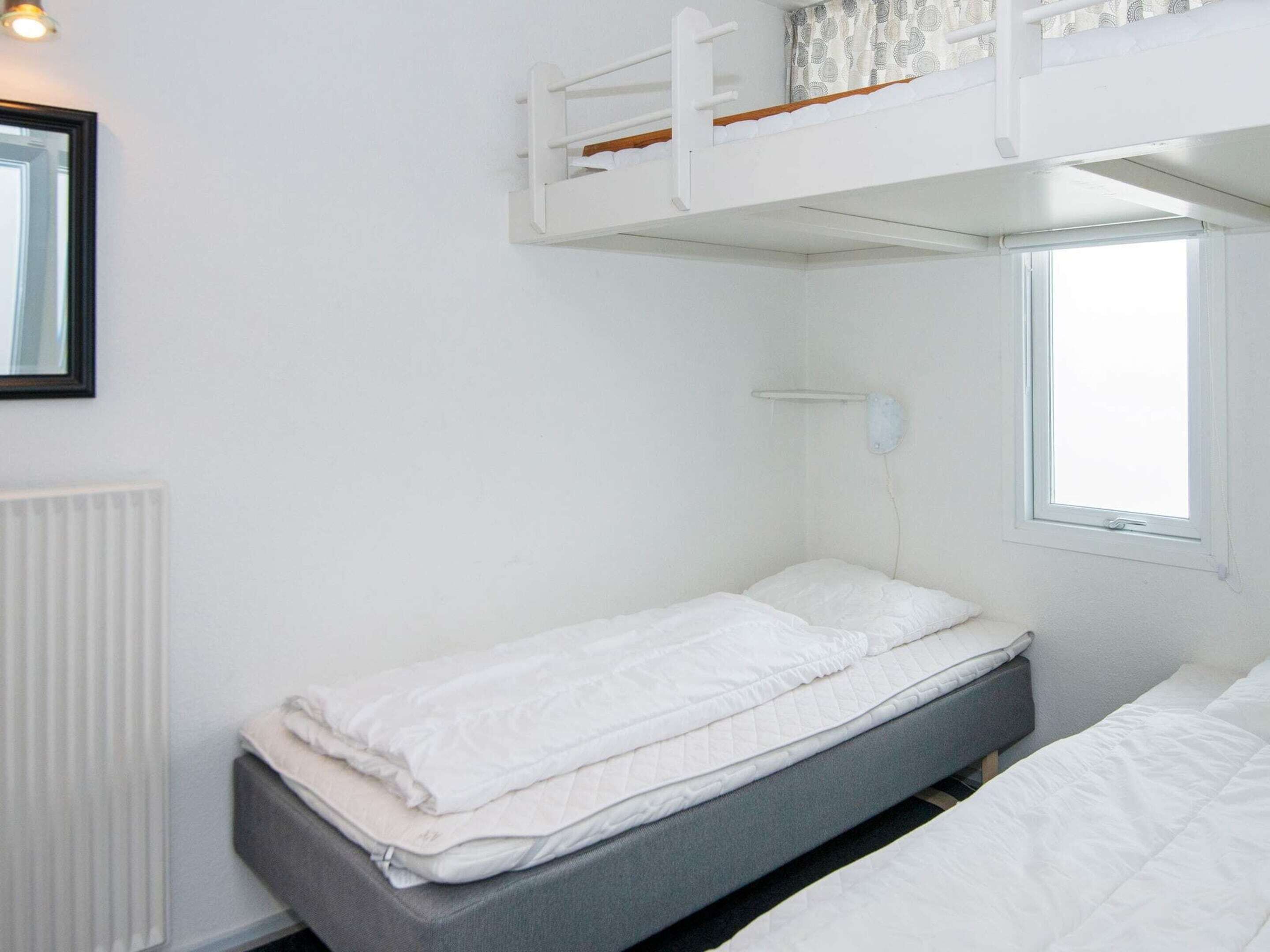 Een slaapkamer met stapelbed, raam, radiator en een lijst met een afbeelding aan de muur.