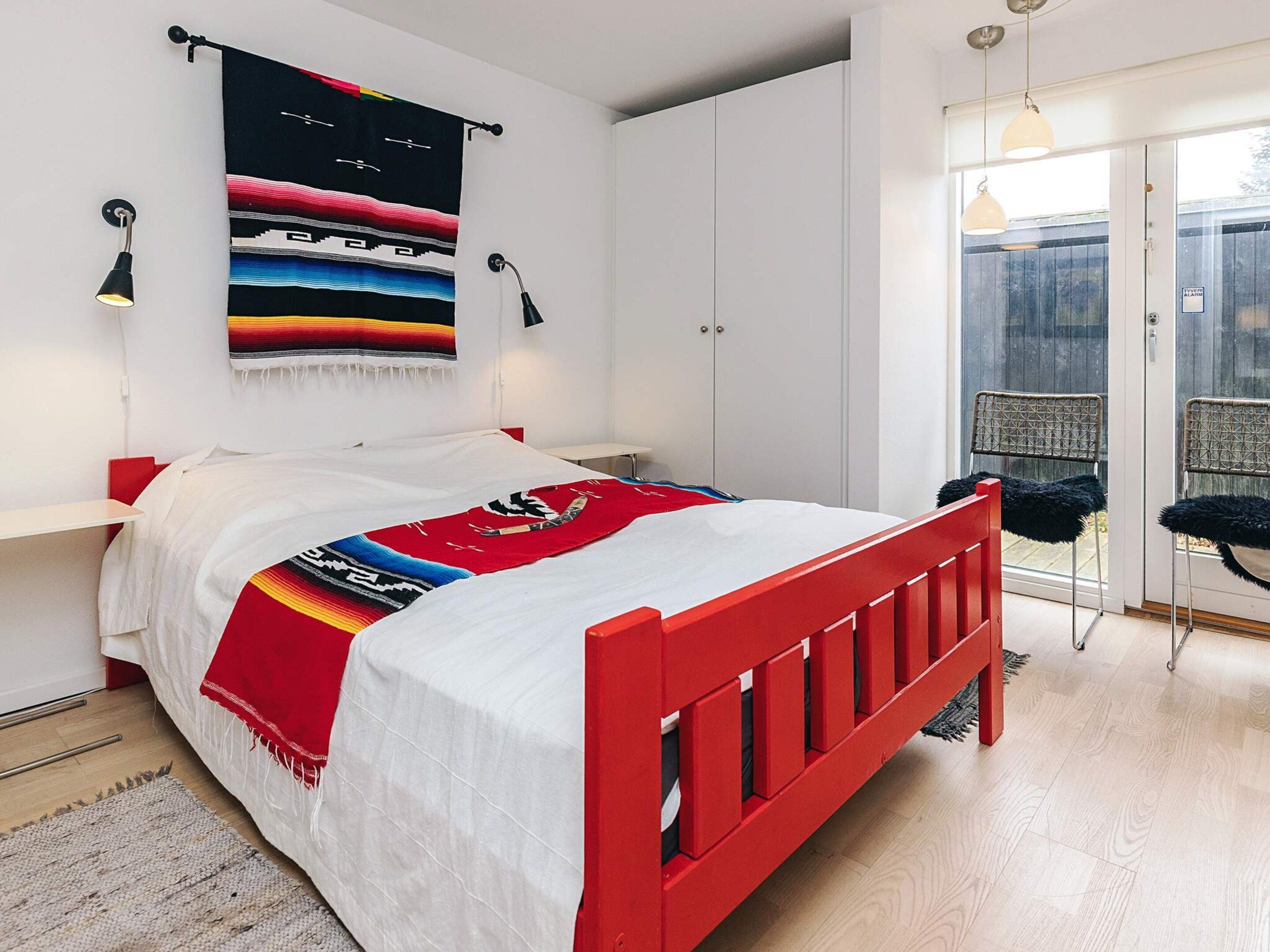 Un dormitorio con una cama, cabecera roja, tapiz colgado en la pared y una ventana con vistas.