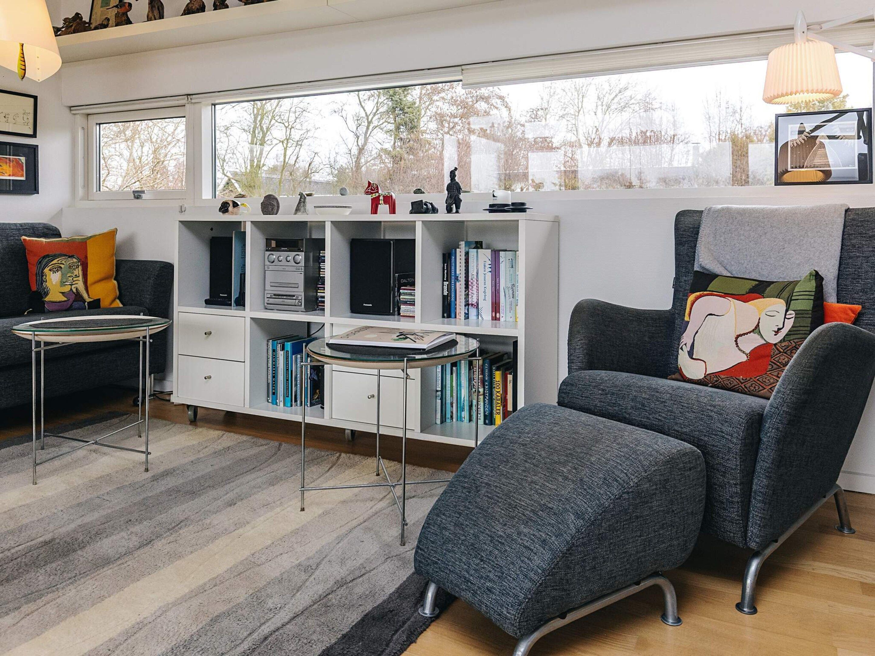 A modern living room with a sofa, a small table, a bookshelf, and a large window.