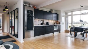 Une cuisine moderne avec des meubles de couleur sombre, un réfrigérateur en acier inoxydable et un coin repas comprenant une table et des chaises.