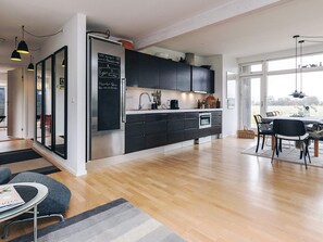 Una cocina moderna con armarios oscuros, un refrigerador de acero inoxidable y un comedor con mesa y sillas.