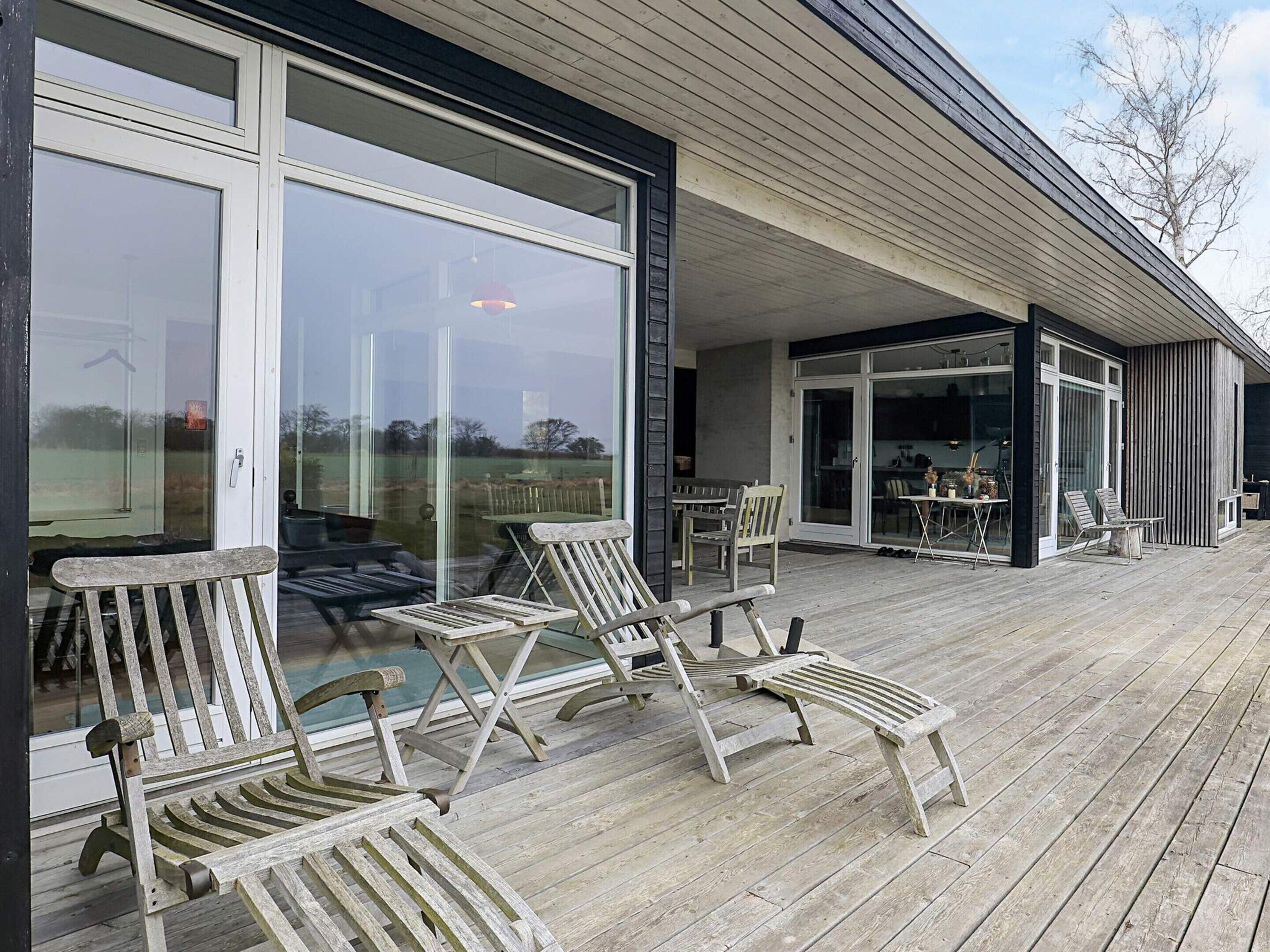 Une terrasse en bois avec des sièges extérieurs et de grandes portes vitrées donnant sur un espace intérieur.