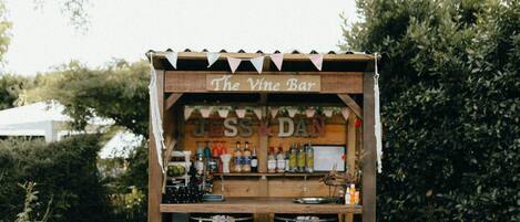 A rustic outdoor bar setup with wooden barrels and stools, featuring a sign that reads "The Vine Bar."