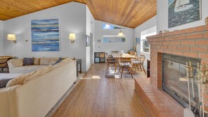 A spacious living area with a wooden ceiling, a fireplace, and a dining table with chairs. - 2 Blocks to Beach | Firepit | Sandbox | BBQ | Work (Carlsbad)