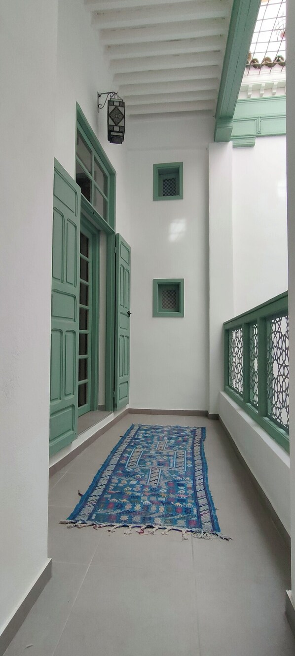 Um corredor com portas verdes, um tapete estampado e um ventilador de teto.