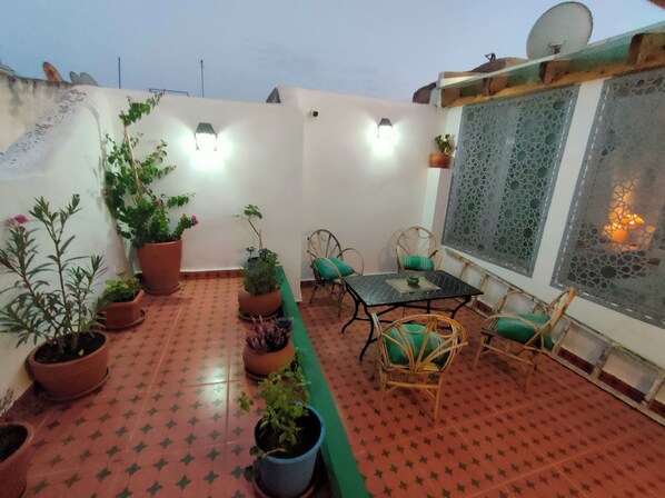 Eine Dachterrasse mit Tisch und Stühlen, Topfpflanzen und einer Zierwand.