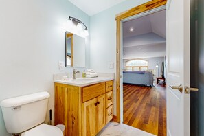 A bathroom with a wooden vanity, a white toilet, and a mirror with lights. - Beautiful home in wine country w/ deck, peaceful views & close to town (Penn Yan)