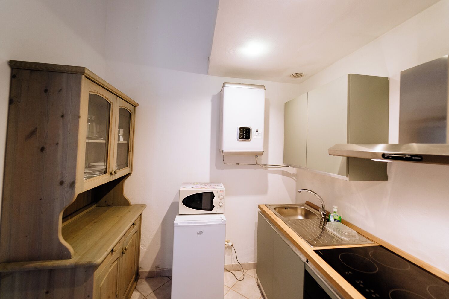 Una cocina compacta con microondas, un refrigerador pequeño, un lavamanos con grifo y armarios de madera.