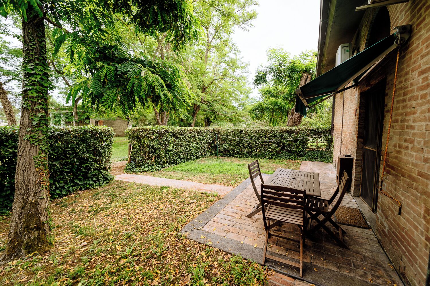 A patio with a table and chairs, surrounded by a brick wall and a hedge.
