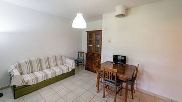 Una sala de estar con sofá, mesa de comedor con sillas, aparador y televisor.