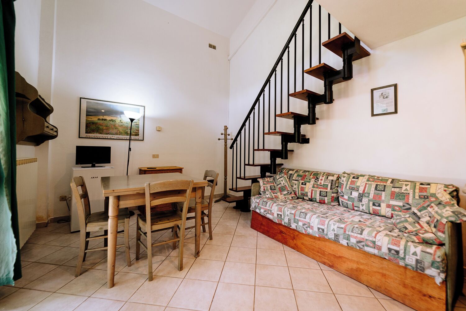 Una sala de estar con una mesa de comedor de madera, sillas, un sofá y una escalera con barandas negras.