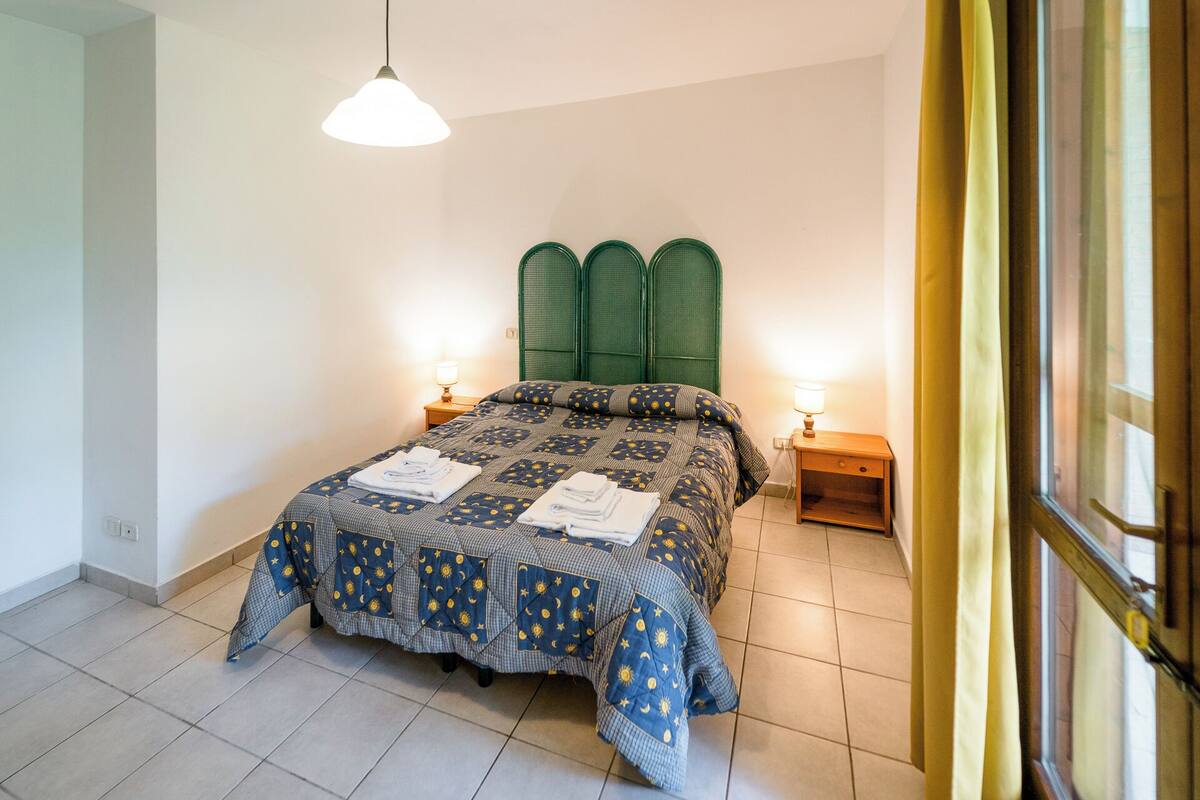 A bedroom with a bed, two bedside tables, a hanging light, and a window with curtains.