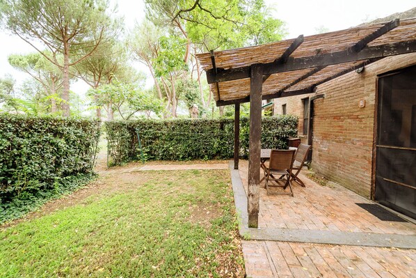 Zona patio con muro in mattoni, una pergola in legno e un tavolo con sedie.