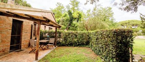 A brick building with a patio area, a wooden table and chairs, and a well-maintained hedge.