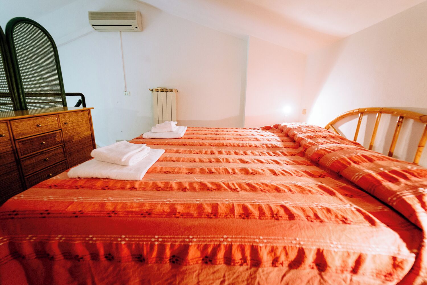 Un dormitorio con una cama, un aparador de madera, un radiador y un equipo de aire acondicionado.