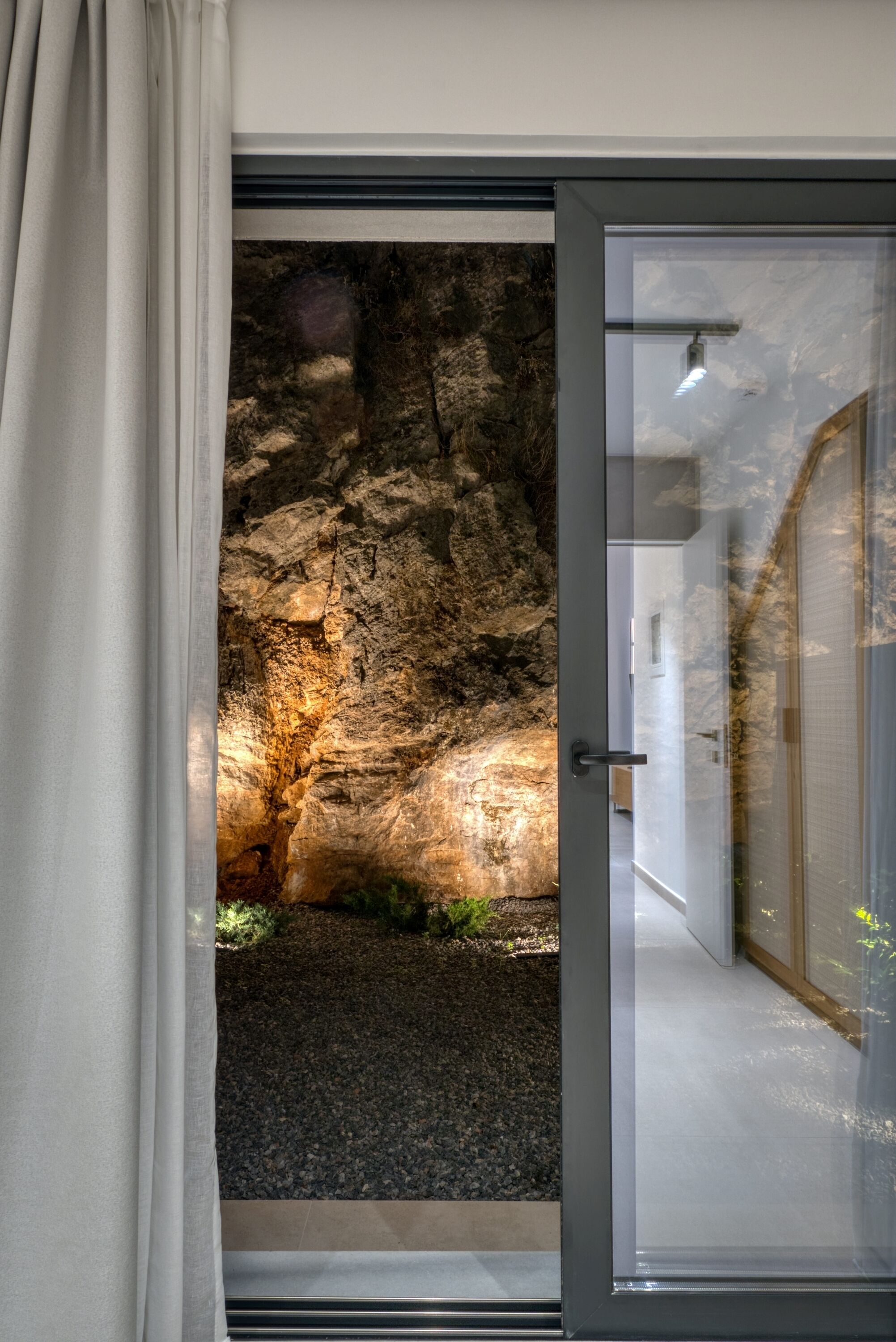A modern interior with a glass door leading to a natural rock formation.
