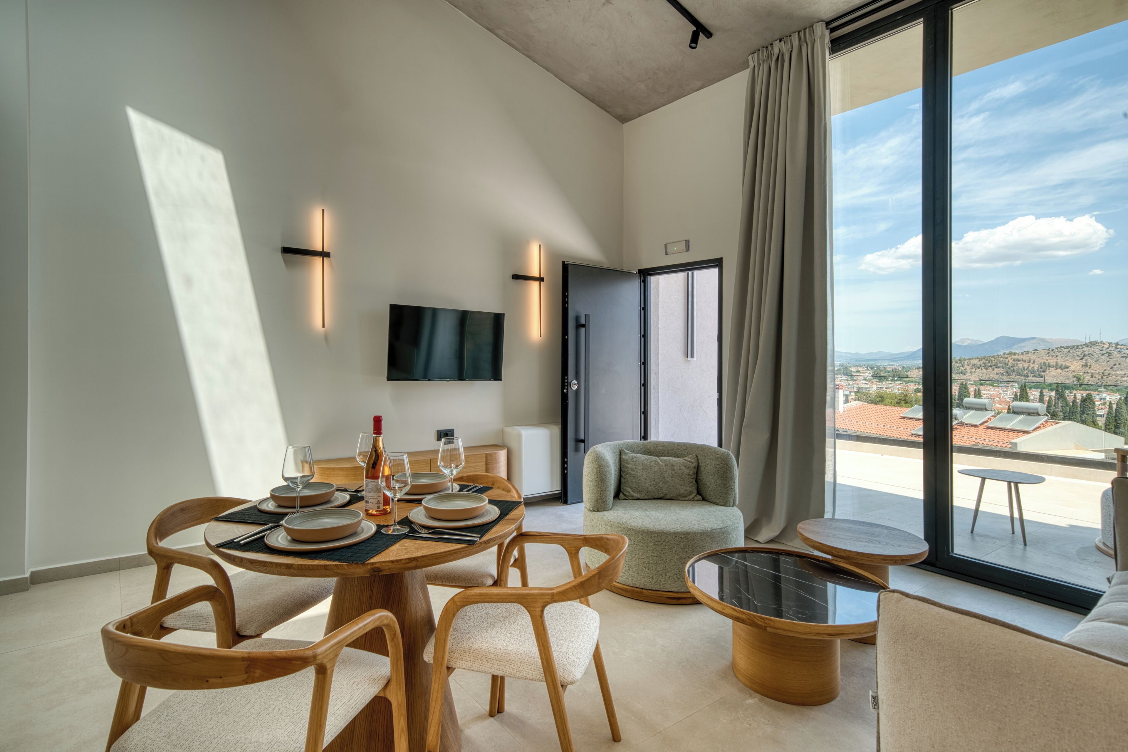 Zona de menjador moderna amb una taula rodona, cadires de fusta i vista a la ciutat a través de grans finestres.