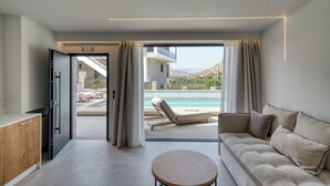 Een moderne woonkamer met een bank, een ronde tafel en uitzicht op een buitenzwembad en bergen.