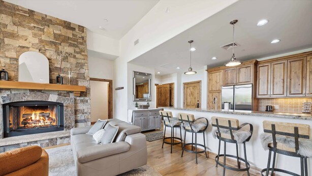 A modern living room with a fireplace, a sofa, and a coffee bar with stools. - Beaver Creek Landing A408 (Beaver Creek)