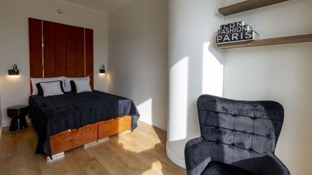 A bedroom with a bed, a black chair, a wardrobe, and a sign on the wall. - Apartment in Szczecin With Pool and Terrace (Szczecin)