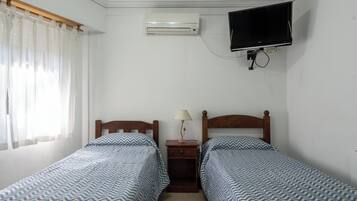 Un dormitorio con dos camas, un televisor montado en la pared y un aire acondicionado.