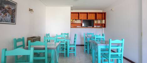 A dining area with turquoise chairs and tables, a kitchen with wooden cabinets, and a painting on the wall.