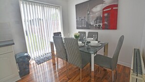 Uma área de refeições com uma mesa de vidro, cadeiras estofadas cinzentas e um quadro de uma cabine telefônica vermelha.