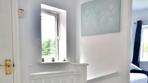Quarto com teto branco, janela com vista, cama com roupa de cama azul e obra de arte pendurada na parede.