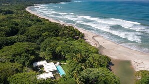A coastal landscape with a beach, dense greenery, and a building with a pool. - Oceanfront Paradise:4-Bedroom Villa with Expansive Pool in Santa Teresa Sea Wing (Puntarenas Province)
