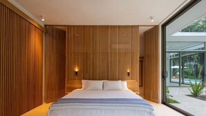 A modern bedroom with a large bed, wooden panel walls, and a glass door leading to an outdoor area. - Oceanfront Paradise:4-Bedroom Villa with Expansive Pool in Santa Teresa Sea Wing (Puntarenas Province)