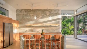 A modern kitchen with a marble backsplash, a stainless steel refrigerator, and wooden chairs. - Oceanfront Paradise:4-Bedroom Villa with Expansive Pool in Santa Teresa Sea Wing (Puntarenas Province)
