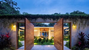 A modern house with a wooden archway leading to a well-lit interior. - Oceanfront Paradise:4-Bedroom Villa with Expansive Pool in Santa Teresa Sea Wing (Puntarenas Province)