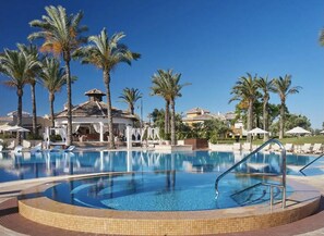 A pool area with lounge chairs and palm trees, surrounded by buildings with tiled roofs. - 3 Bed Villa/mar Menor Golf/heated Pool/terrace (Torre-Pacheco)